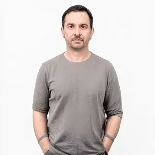 A man standing straight facing the camera, hands in pockets,