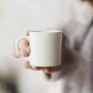 A person holding a white ceramic coffee mug by the handle wi