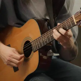 A person playing an acoustic guitar with left hand on the fr