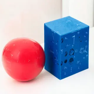 A red ball and a blue cube sitting side by side on a white s