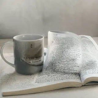 A coffee mug next to an open book on a desk