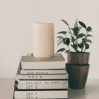 A candle on top of a stack of books, the books next to a pot