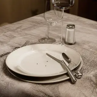 A dinner table scene with a plate, fork, knife, wine glass, 