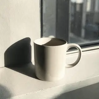 A coffee mug on a sunny windowsill casting a sharp shadow to