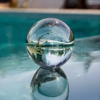 A clear glass sphere sitting on a mirror surface near a pool