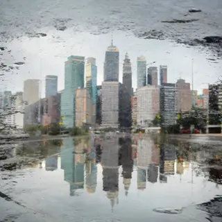 A city skyline reflected in a rain puddle on a street, with 