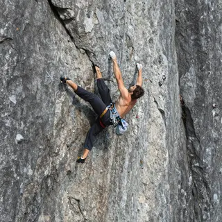 A rock climber clinging to a cliff face with arms and legs e