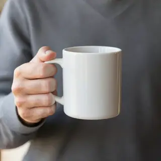 A person holding a white ceramic coffee mug by the handle wi