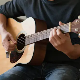 A person playing an acoustic guitar with left hand on the fr