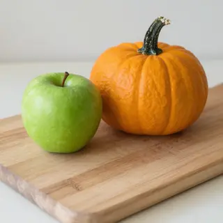 A green apple and an orange pumpkin on a wooden cutting boar