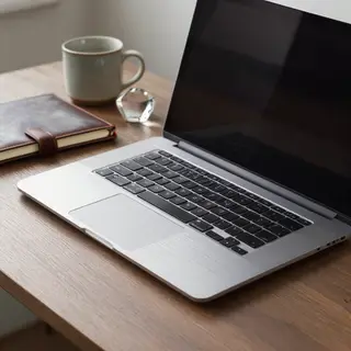 A workspace desk with a brushed aluminum laptop, a leather-b