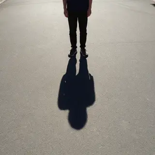 A person standing outdoors at midday with a short shadow dir