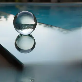 A clear glass sphere sitting on a mirror surface near a pool