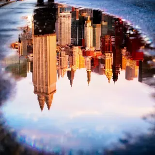 A city skyline reflected in a rain puddle on a street, with 