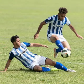 Two soccer players mid-tackle, one sliding and the other jum