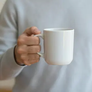 A person holding a white ceramic coffee mug by the handle wi