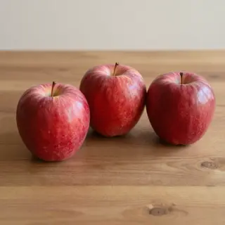 Exactly 3 red apples arranged on a wooden table
