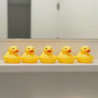 Exactly 5 yellow rubber ducks sitting in a row on a bathroom