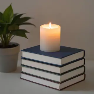 A candle on top of a stack of books, the books next to a pot