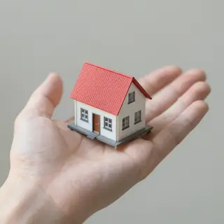 A miniature house sitting on the palm of someone's hand