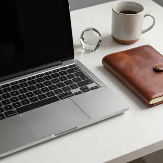 A workspace desk with a brushed aluminum laptop, a leather-b