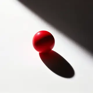 A red sphere on a white surface with a single shadow cast to