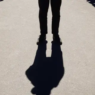 A person standing outdoors at midday with a short shadow dir