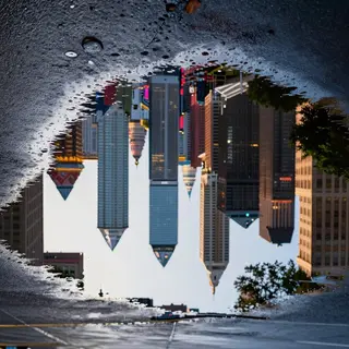 A city skyline reflected in a rain puddle on a street, with 