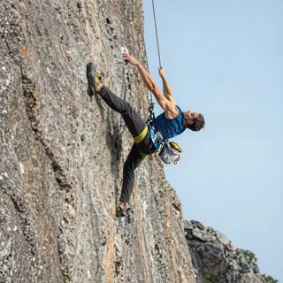 A rock climber clinging to a cliff face with arms and legs e