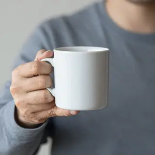 A person holding a white ceramic coffee mug by the handle wi