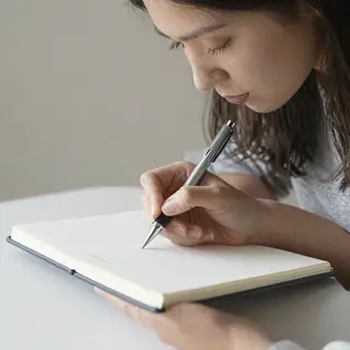 A woman writing in a notebook with a pen gripped correctly i