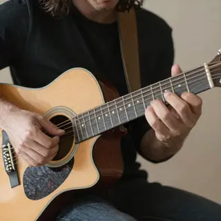 A person playing an acoustic guitar with left hand on the fr