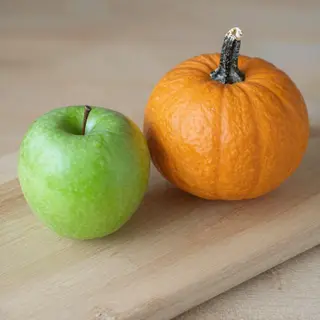 A green apple and an orange pumpkin on a wooden cutting boar