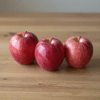 Exactly 3 red apples arranged on a wooden table