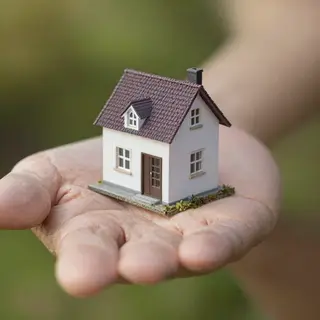 A miniature house sitting on the palm of someone's hand