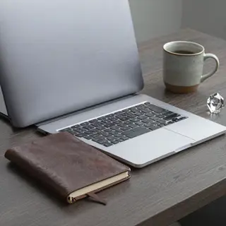 A workspace desk with a brushed aluminum laptop, a leather-b