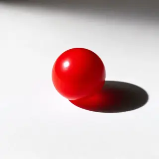 A red sphere on a white surface with a single shadow cast to
