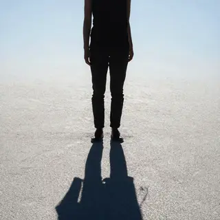 A person standing outdoors at midday with a short shadow dir