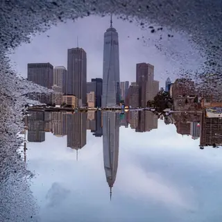 A city skyline reflected in a rain puddle on a street, with 