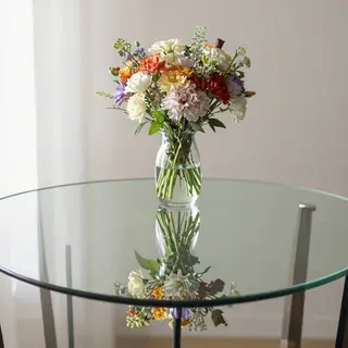 A vase of flowers on a glass table with a clear reflection v