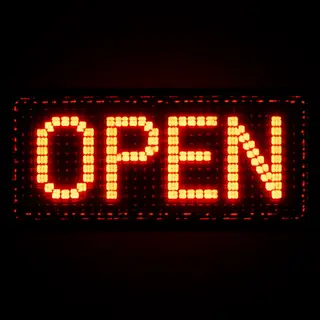 The word 'OPEN' displayed on a red LED sign with glowing pix