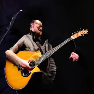 A person playing an acoustic guitar with left hand on the fr