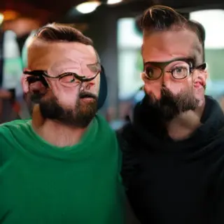 Two men at a cafe: one with a beard and glasses wearing a gr