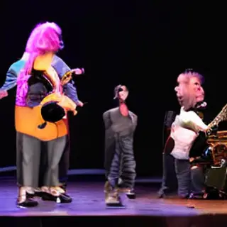 Three musicians on stage: a tall woman with short pink hair 