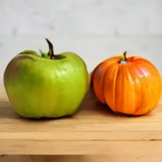 A green apple and an orange pumpkin on a wooden cutting boar