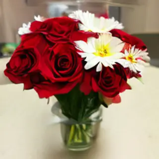 4 red roses and 2 white daisies in a glass vase on a table