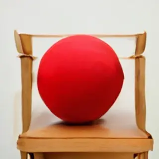 A red ball underneath a wooden chair
