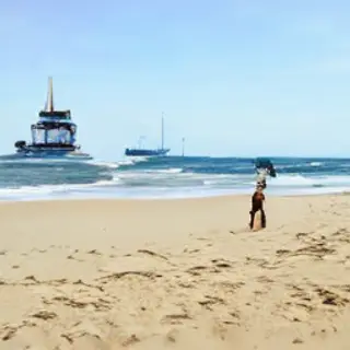 A beach scene with a sandcastle in the foreground, a surfer 