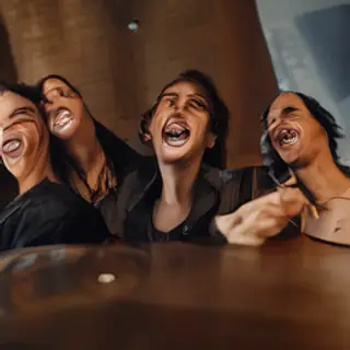 A group of three friends at a table: one laughing with head 