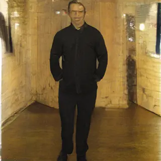 A man standing straight facing the camera, hands in pockets,